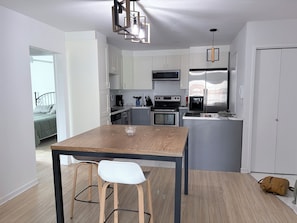 A modern kitchen with white cabinets, a wooden dining table, and bar stools. - Cozy 2-bedroom apartment 22 minutes from Montreal (La Prairie)