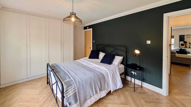 Una camera da letto con un letto, comodino, lampada, armadio e vista su un'altra stanza.