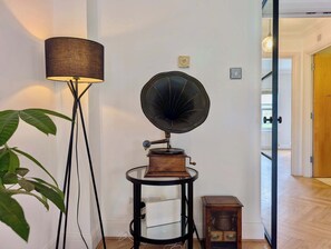 Ein Zimmer mit Stehlampe, Grammophon, einem kleinen Tisch mit einem weißen Gerät und einem Holzschrank.