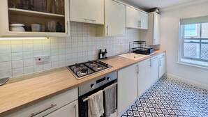 Una cucina moderna con mobili bianchi, piano cottura a gas, lavello e piastrelle decorative.