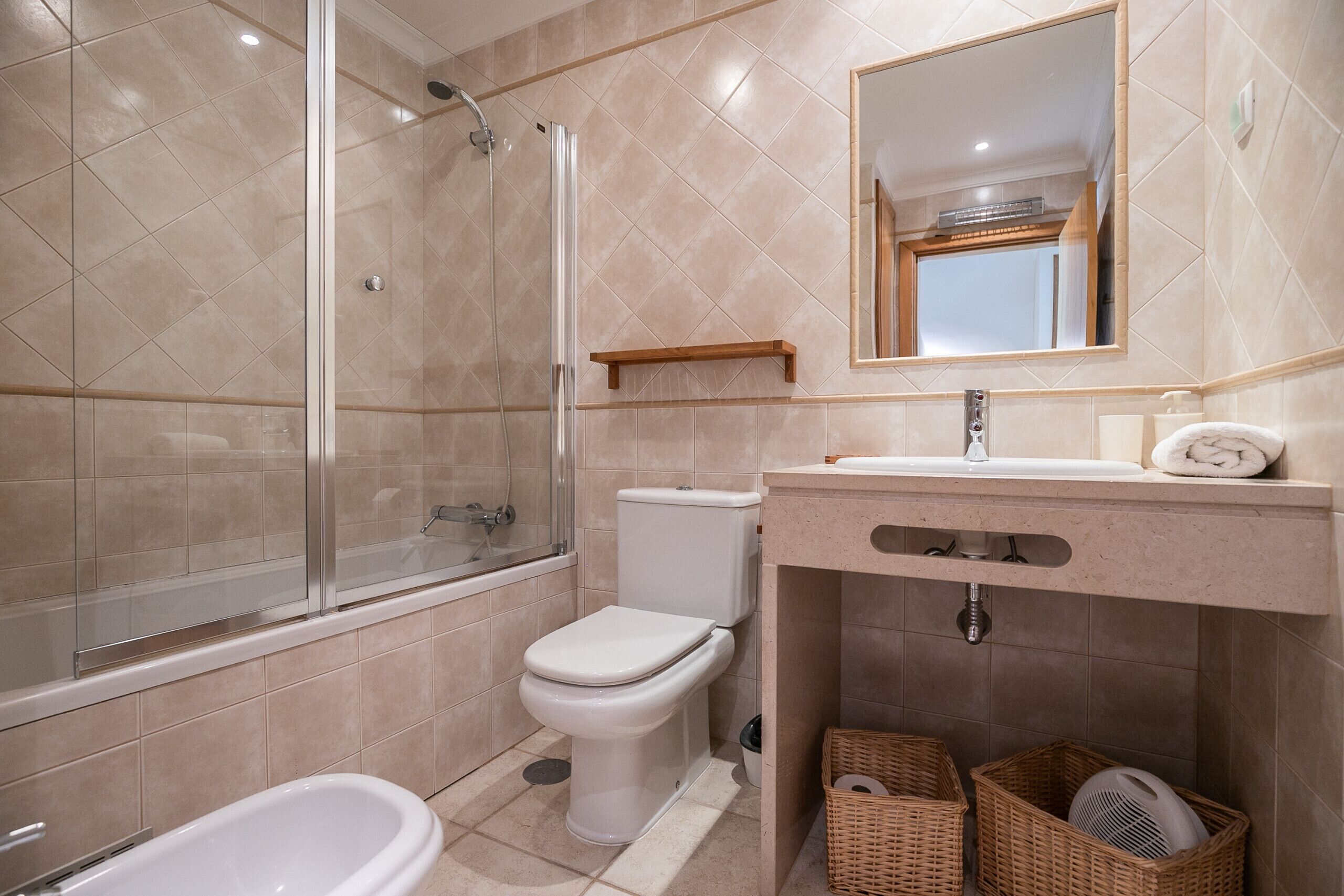 Un bagno con doccia vetro, un water, un lavandino con specchio e cesti in vimini.