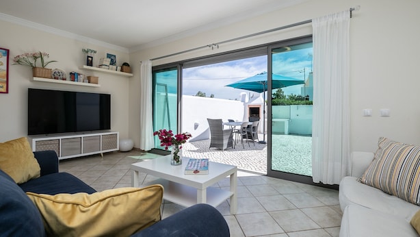 A living room with a TV, sofa, coffee table, and a view of the outdoor patio area. - Moradia V3 a 100m da praia by ALGARVEMANTA (24V3) (Manta Rota)