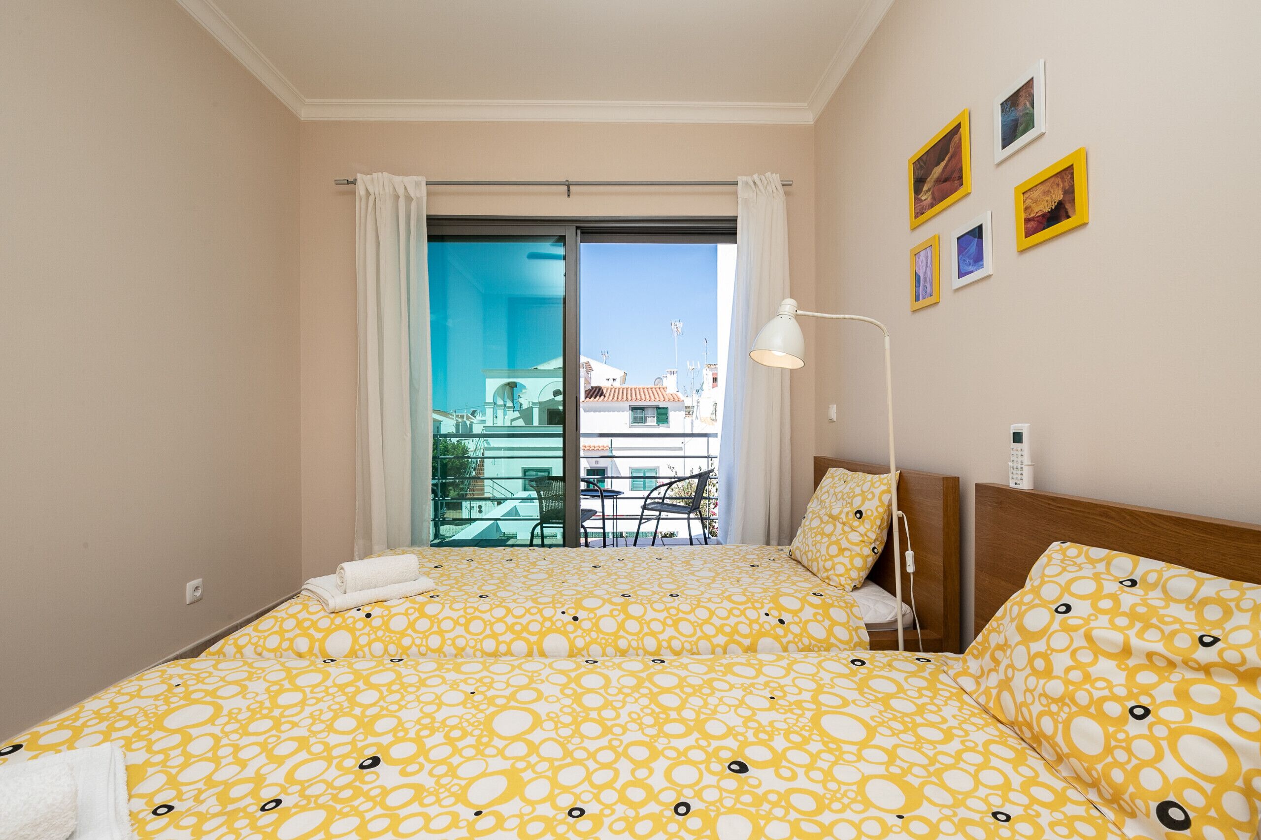 Un cuarto de hotel con una cama, una mesita de noche, una lámpara y vista al exterior.