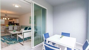 En moderne stue med en hvid sofa, blå stole, et hvidt bord og en glas skydedør ind til et køkken.