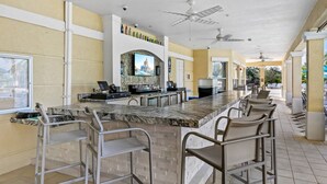 Eine Bar mit Marmorplatte, Barhocker, einem Fernseher und einem Deckenventilator.