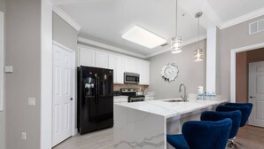 A modern kitchen with white cabinets, a black refrigerator, a microwave, a stove, and a bar area with blue bar stools. - Vista Cay Home Near Universal, Pool & Lake (Orlando)