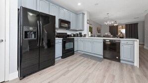 A modern kitchen with light blue cabinets, a black refrigerator, a microwave, an oven, and a dishwasher. - Vista Cay 3BR Near Universal & Disney Parks (Orlando)