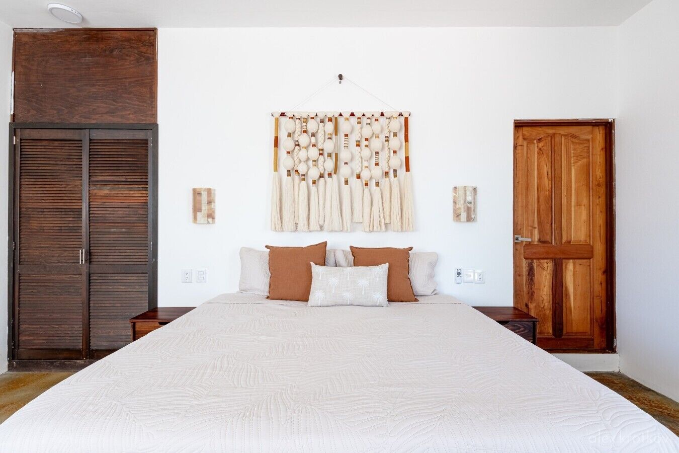 A bedroom with a large bed, wooden wardrobe, and a wall-mounted tapestry.