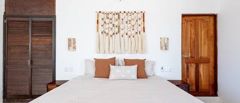 A bedroom with a large bed, wooden wardrobe, and a wall-mounted tapestry.