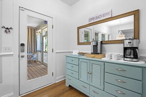 Una habitación con cafetera, espejo, puerta que da a un balcón y cómoda azul claro.