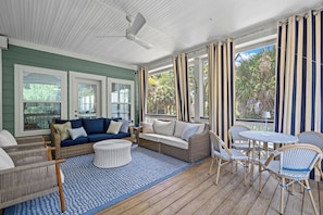 A covered porch with a blue sofa, wicker furniture, and a table with chairs. - Extensive Outdoor Living, Club Cards Available, Golf Cart Included - 507 Remora Circle (Fripp Island)