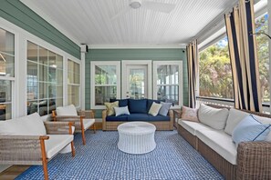 Ein Wintergarten mit blau gemustertem Boden, Korbmöbeln und Blick auf Grünfläche draußen.