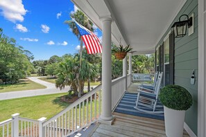 Eine Veranda mit weißem Geländer, einer amerikanischen Flagge, die an einem Haken hängt, und einem Blumentopf.