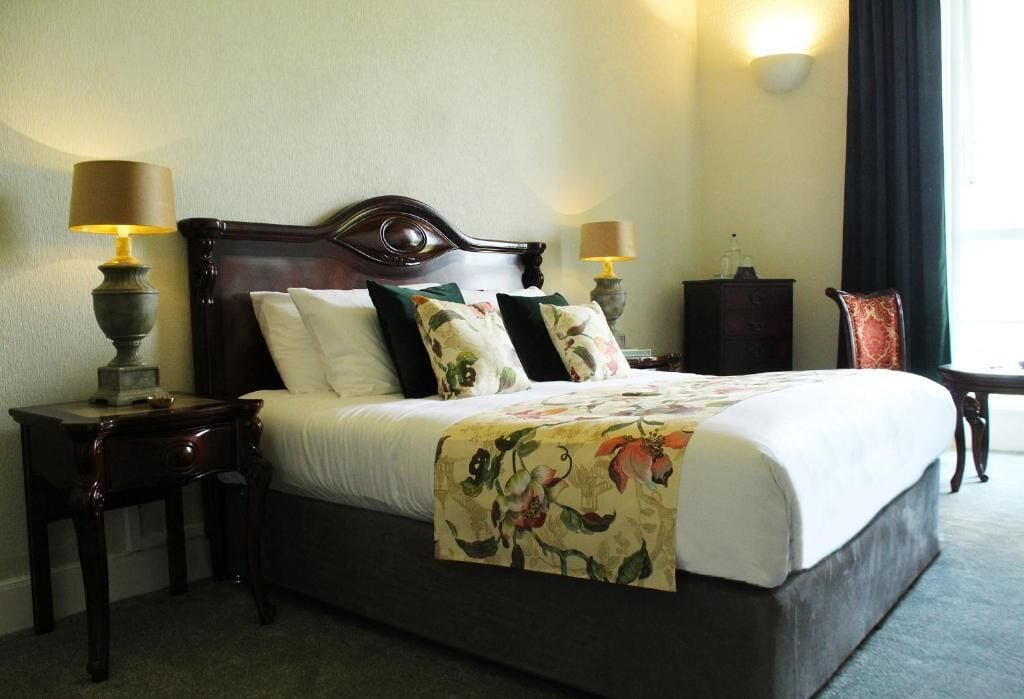 Habitación de hotel con una cama grande, dos mesitas de noche con lámparas, un atril y un escritorio.