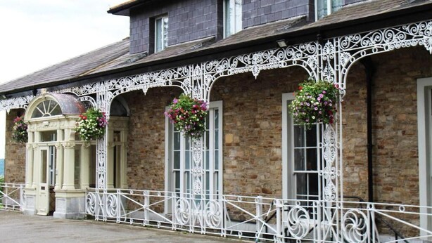 A building with a brick facade, white decorative metal railings, and flower baskets.