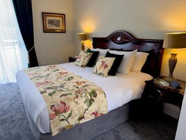 Habitación de hotel con cama, dos lámparas de noche, una mesita de noche, un cuadro en la pared y una ventana con cortinas.