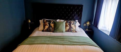 A neatly made bed with a green bedspread and decorative pillows, a dark headboard, and a bedside table with a lamp.