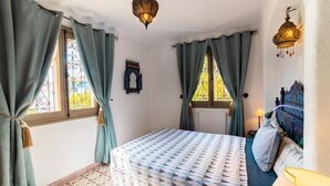 A bedroom with a bed, curtains, a wall-mounted light fixture, and a window with a decorative metal grille.