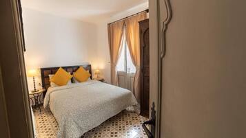 A bedroom with a bed, two bedside tables, a patterned floor, and a window with curtains.