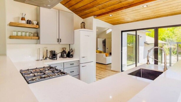 A modern kitchen with white cabinets, a built-in stove, and a wooden ceiling.