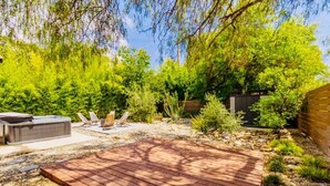 A wooden deck, outdoor seating, and a hot tub in a landscaped garden.
