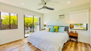 A bedroom with a bed, a ceiling fan, a window with a view, a bedside table, and a nightstand.