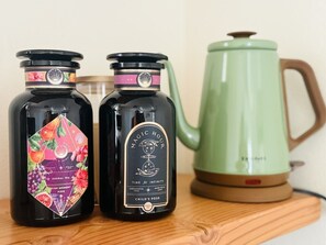 Deux bouteilles noires, toutes deux munies d’une étiquette, et une bouilloire verte, le tout posé sur une surface en bois.