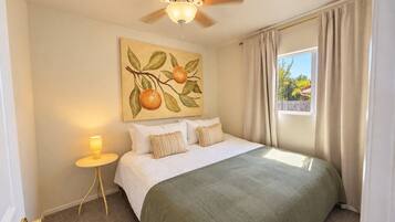 A bedroom with a bed, a nightstand, a ceiling fan, a window with curtains, and a wall painting.