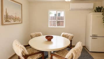 A dining area with a round table, four chairs, a ceiling fan, a window, and a refrigerator.