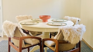 Une table de salle à manger ronde, surmontée d’un saladier rose au centre, entourée de chaises dotées d’accoudoirs recouverts de fourrure.