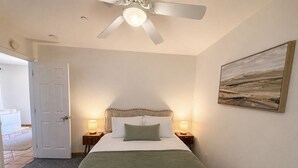 Ein Schlafzimmer mit einem Bett, einem Deckenventilator, einem Gemälde und einer Tür zu einem anderen Raum.