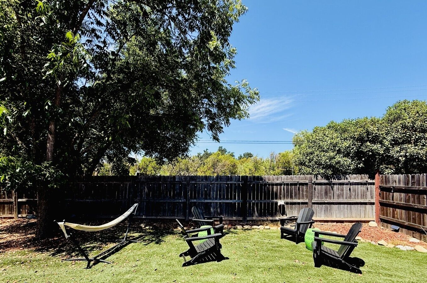 A backyard with a wooden fence, a hammock, and outdoor seating.