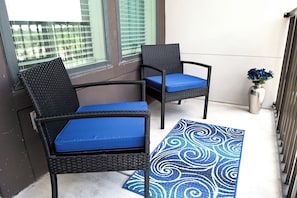 Zwei Korbstühle mit blauen Kissen auf einem Balkon mit einem gemusterten Teppich.