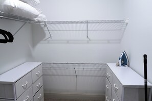 Ein kleiner, weißer Kleiderschrank mit einem Drahtregal darüber und einer weißen Kommode mit Schubladen.