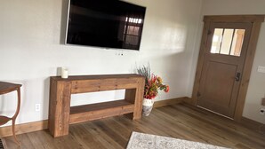 A room with a wooden bench, a flat-screen TV mounted on the wall, a wooden door, and a patterned rug on the floor.
