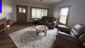 A living room with a ceiling fan, two windows, a sofa, a coffee table, and a door.