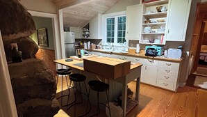 Uma cozinha com ilha de madeira, banquetas e armários brancos.