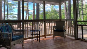 Varanda coberta com móveis de vime, uma pequena mesa e vista para uma área arborizada.