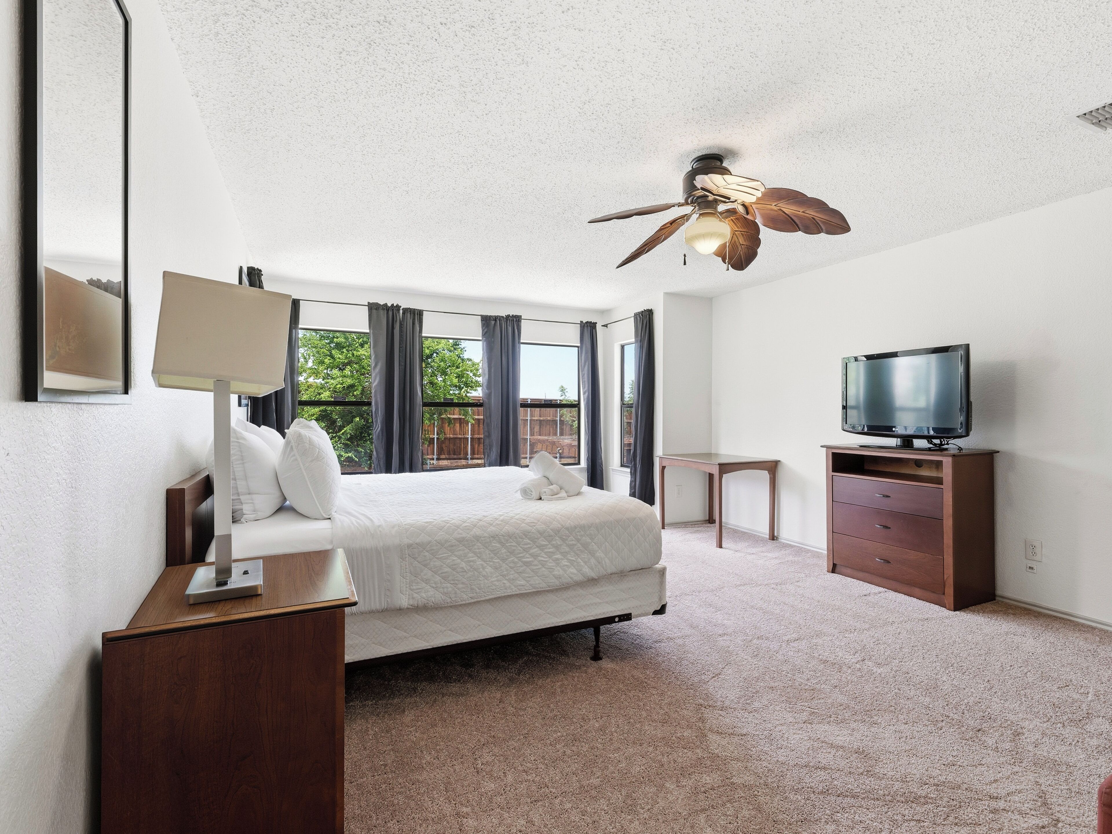 Une chambre à coucher avec un lit, un bureau, une télévision et un ventilateur de plafond.