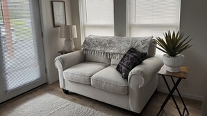 Ein Wohnzimmer mit einer Couch, einer Lampe, einer Pflanze und einem Fenster mit Jalousien.