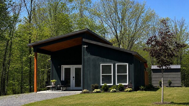 Eine moderne Holzhütte mit überdachter Veranda, einer Tür und einem Fenster.