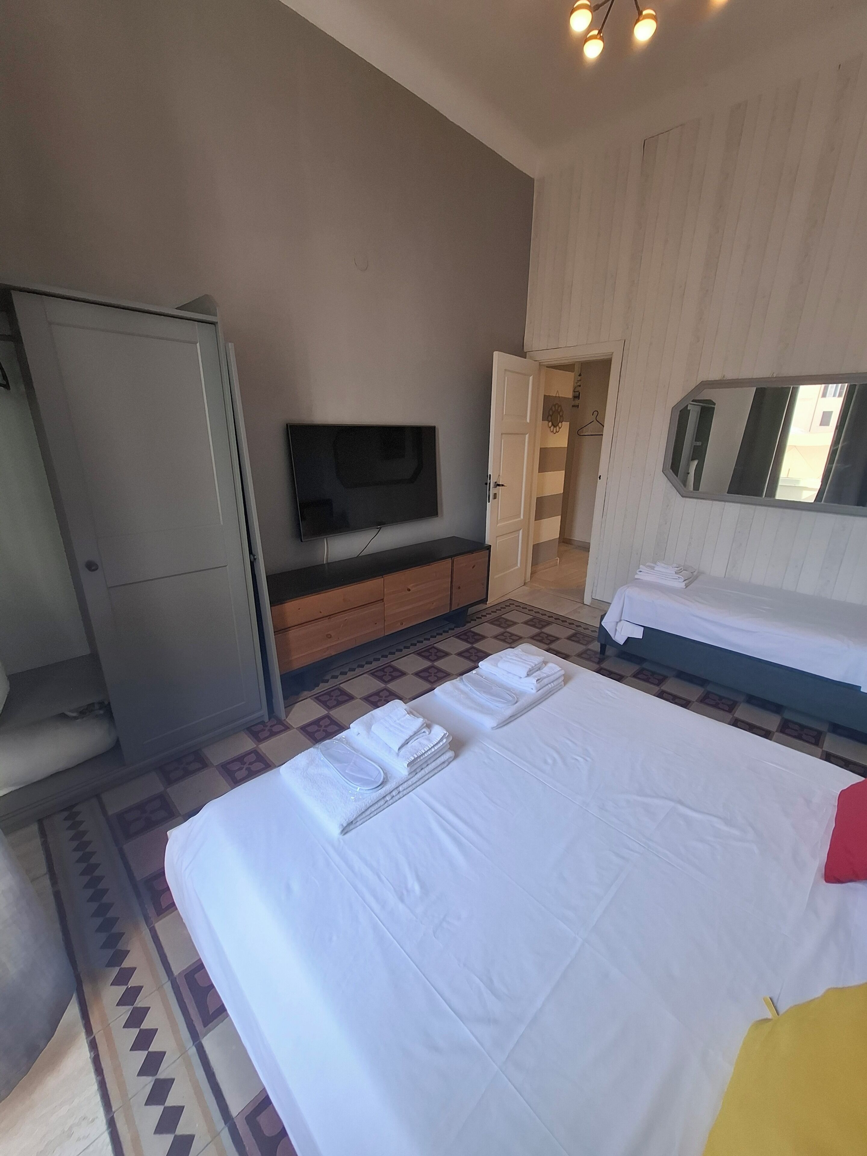 Habitació d'hotel amb un llit, televisió, armari i bany visible a través d'una porta oberta.