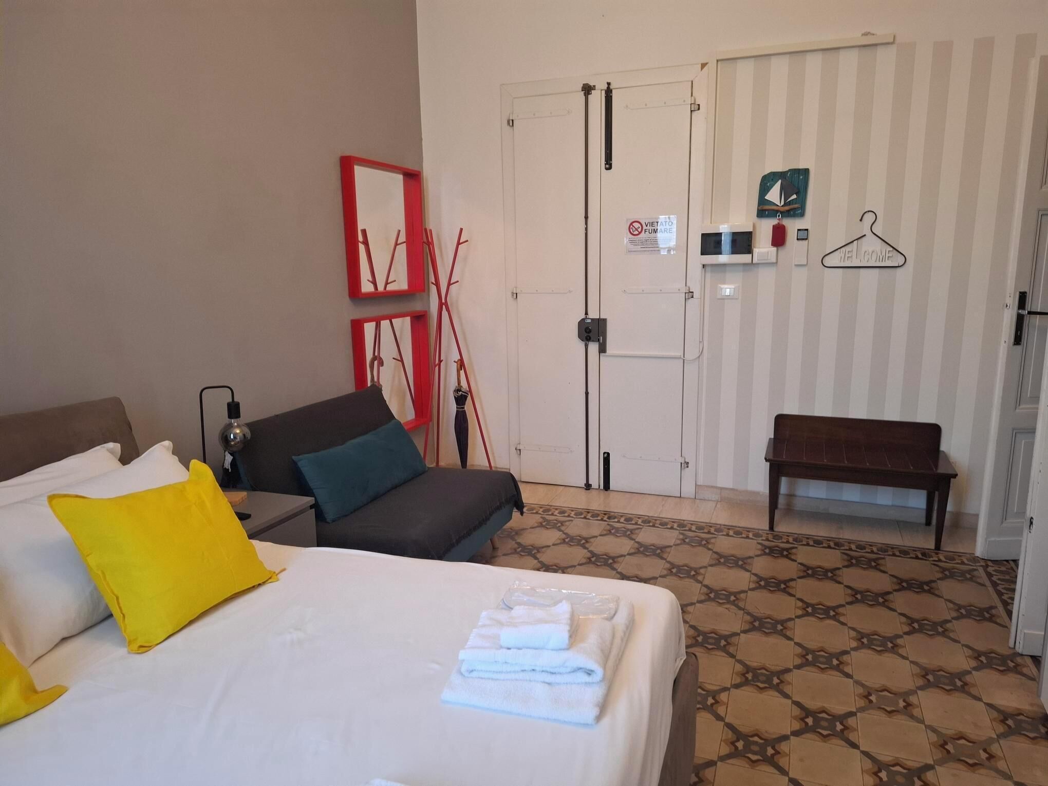 Une chambre d’hôtel avec un lit, un canapé, un banc, un porte-manteau et une porte avec une pancarte.