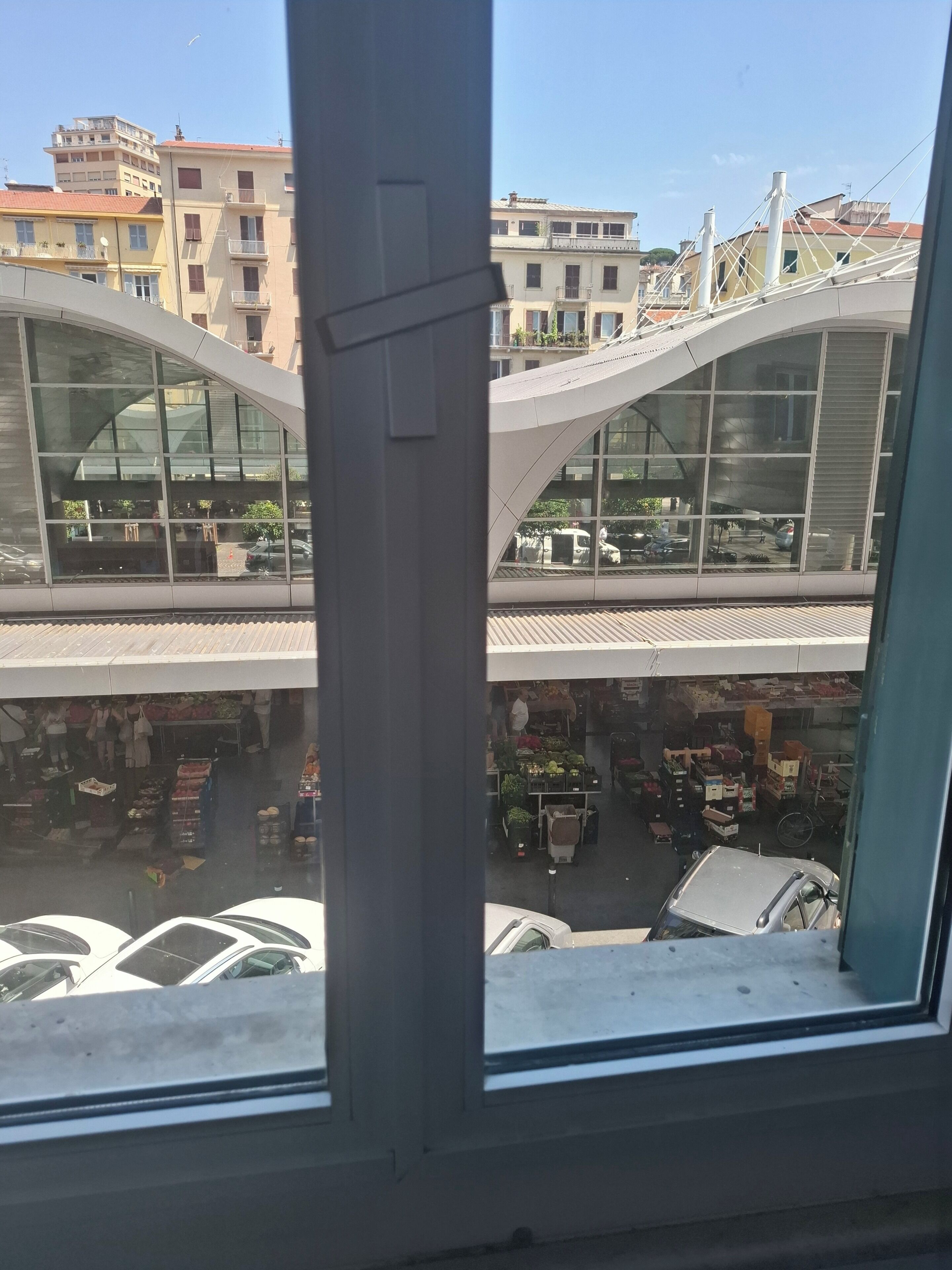 Vista a través de una ventana de un edificio de varios niveles con balcones, un área al aire libre techada y un mercado a nivel de calle con diversos productos.