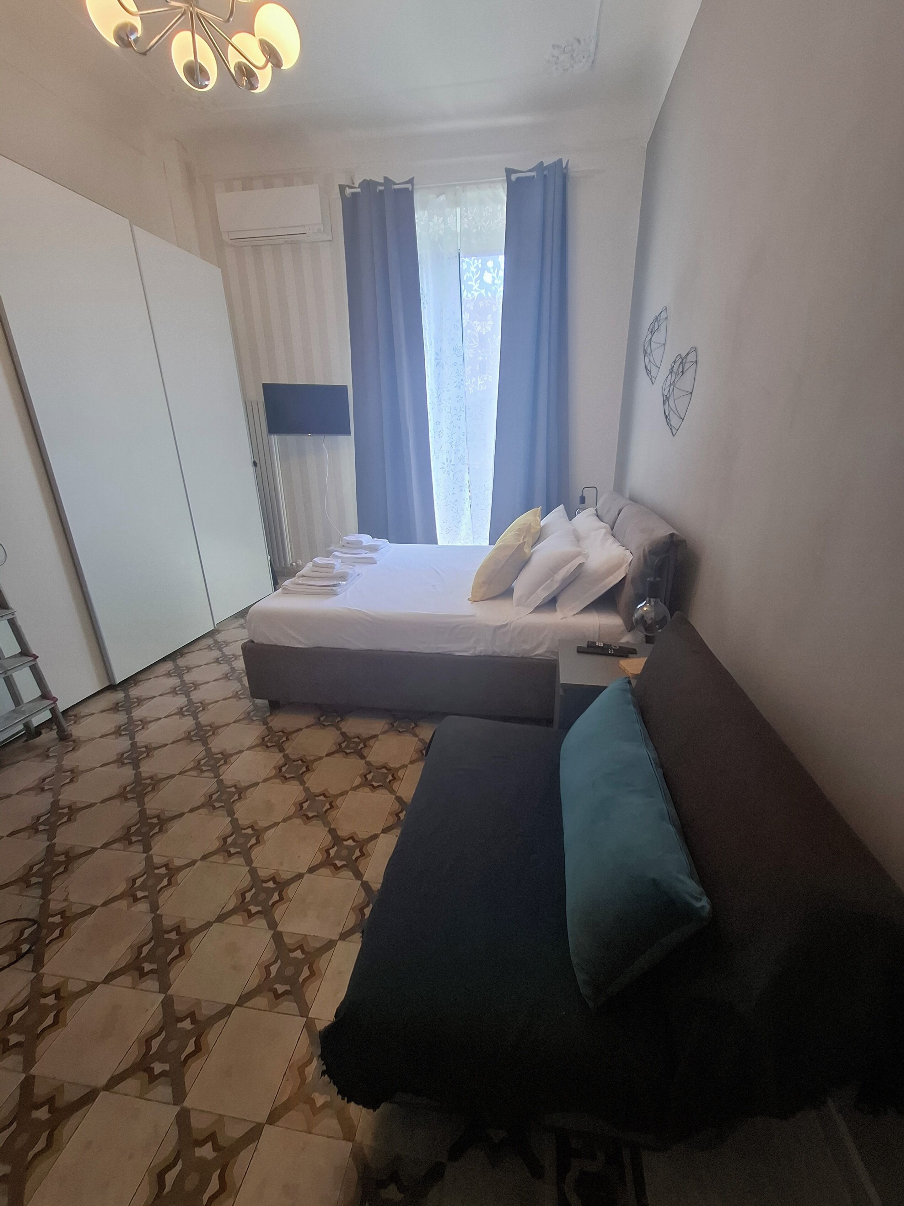 A bedroom with a bed, a sofa, a TV, and a window with curtains.