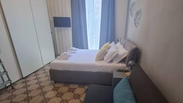A bedroom with a bed, a sofa, a TV, and a window with curtains.
