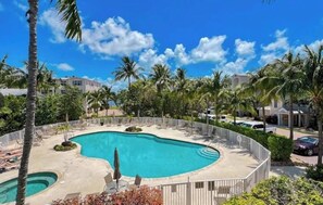 A swimming pool with a curved edge, surrounded by palm trees and lounge chairs, with a clear blue sky above. - Waterfront Condo in Heart of Islamorada, Boat slip (Islamorada)