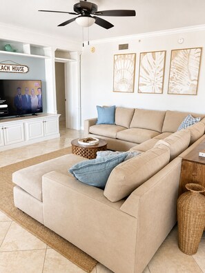 Ein Wohnzimmer mit einem beigen Sofa, einem Fernseher und Wandbildern.