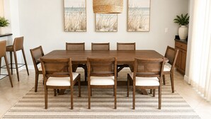 Comedor con una gran mesa de madera, seis sillas, una lámpara colgante de fibra y tres cuadros en la pared.