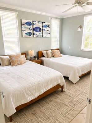 A bedroom with two beds, a ceiling fan, artwork on the wall, and a window with blinds. - Waterfront Condo in Heart of Islamorada, Boat slip (Islamorada)